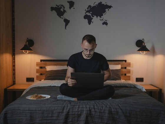 Homem trabalhando em cima da cama com um prato de comida