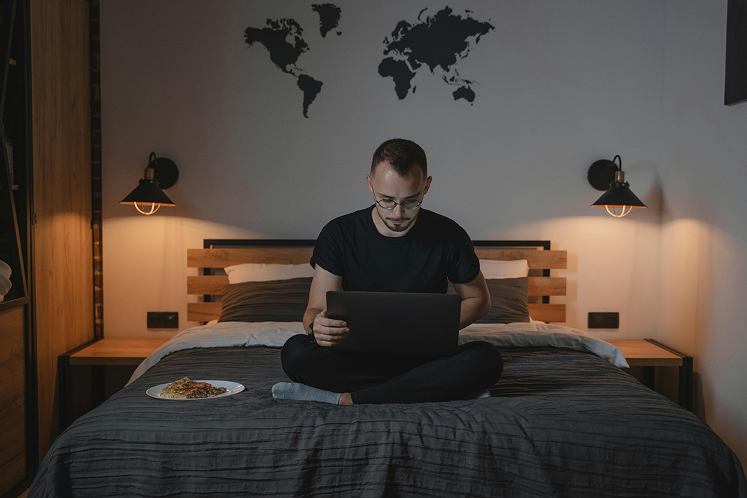 Homem trabalhando em cima da cama com um prato de comida